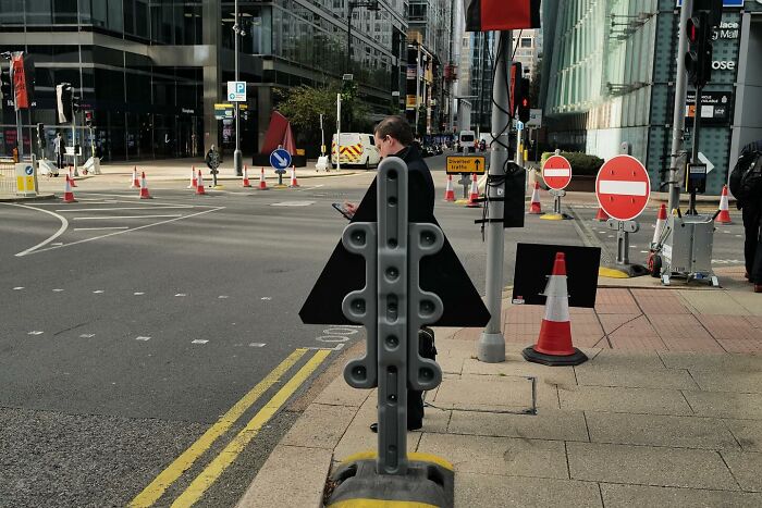 Man standing behind a street sign on a city sidewalk, a humorous street photo capturing the funny side of life.