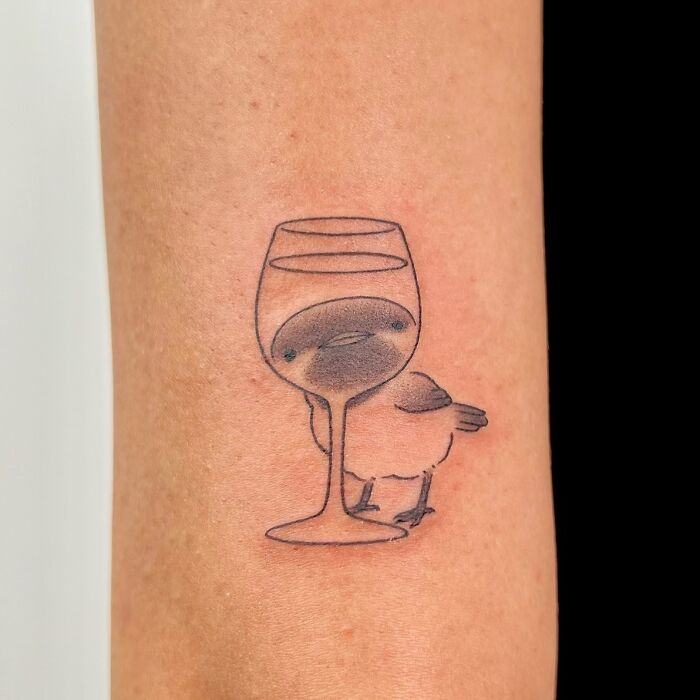 Minimalistic animal tattoo of a bird behind a wine glass with distorted face by Korean artist Buoy on forearm.