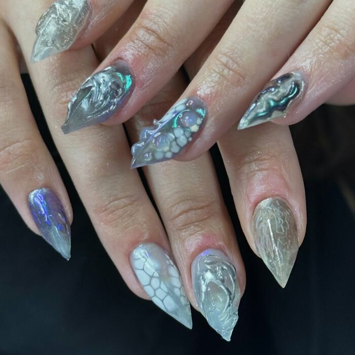 Close-up of unique 3D nail designs featuring textured silver and blue patterns showcasing creative nail art trends.