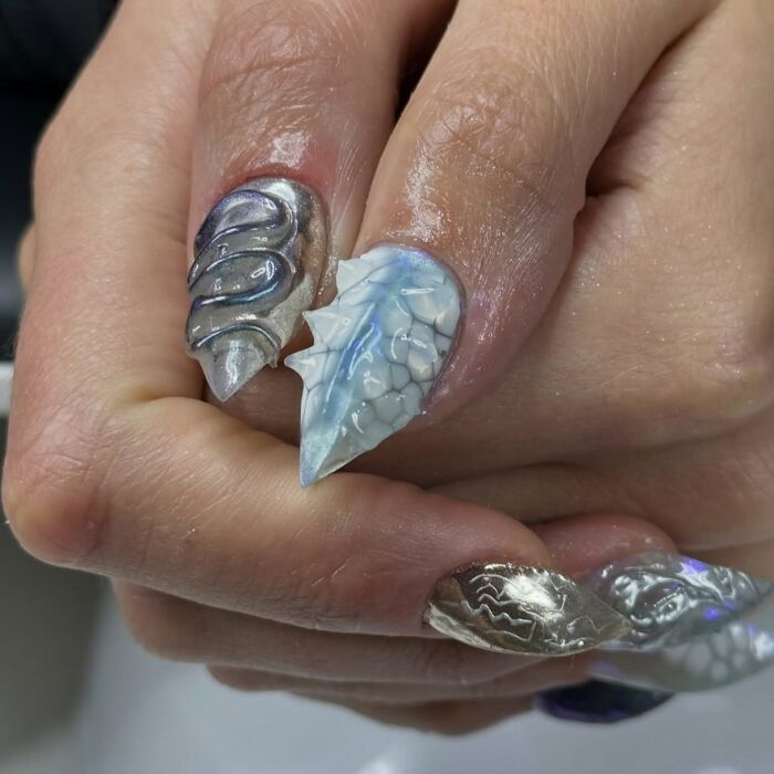 Close-up of unique 3D nail designs featuring textured silver and blue patterns showcasing creative nail art trends.