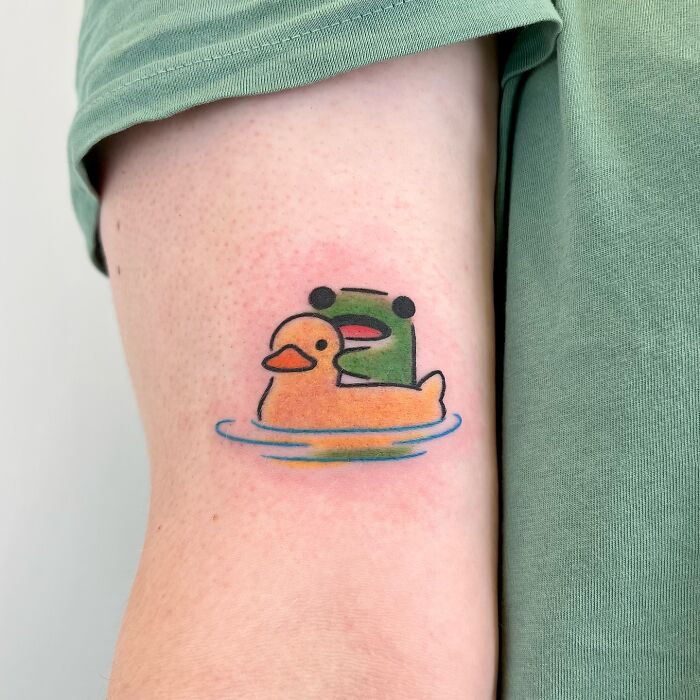 Small adorable frog tattoo with a cute orange duck floating on water inked on a person's arm by Korean artist Buoy.