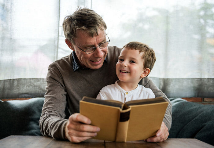 Elderly man and young boy sharing a joyful moment while reading a book, hinting at family secrets revealed.