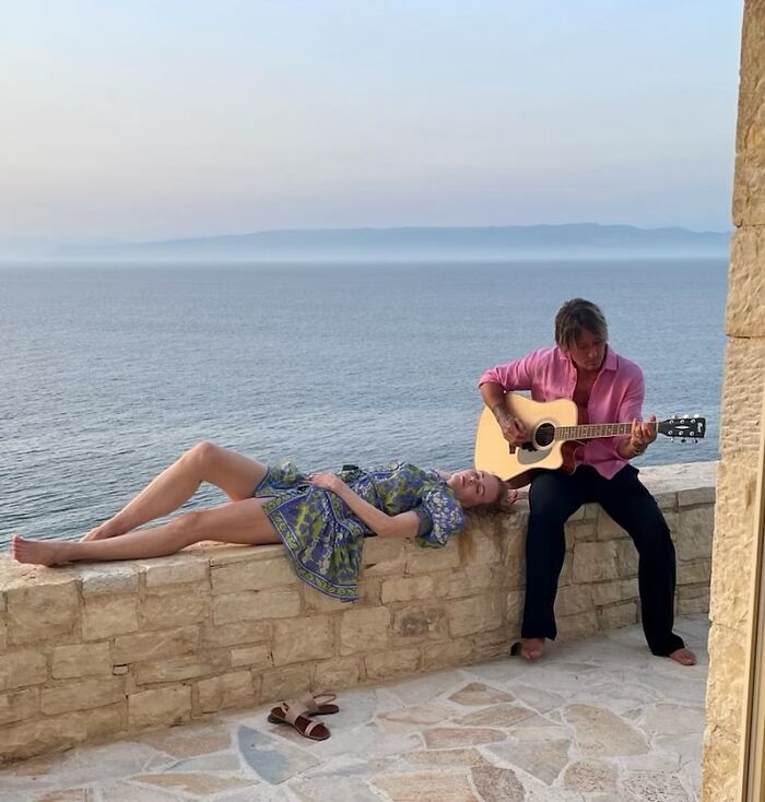 Nicole Kidman lying on stone wall near ocean while Keith Urban plays guitar sitting beside her in casual attire