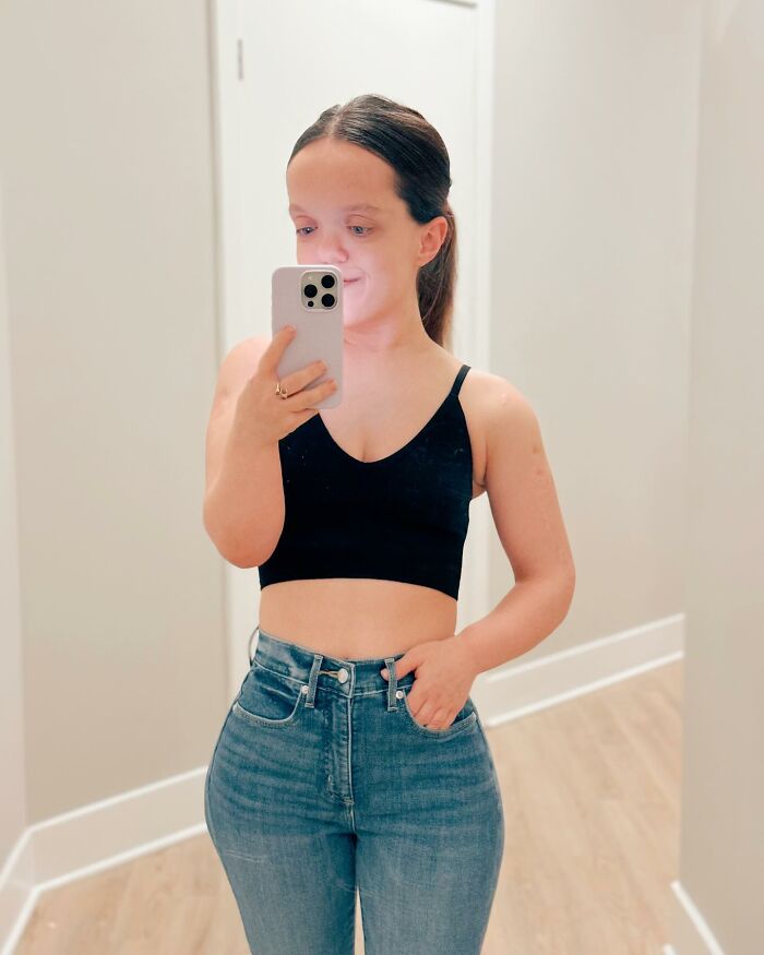 31YO woman with dwarfism taking a mirror selfie wearing black crop top and high-waisted jeans showing transformation after height surgery.