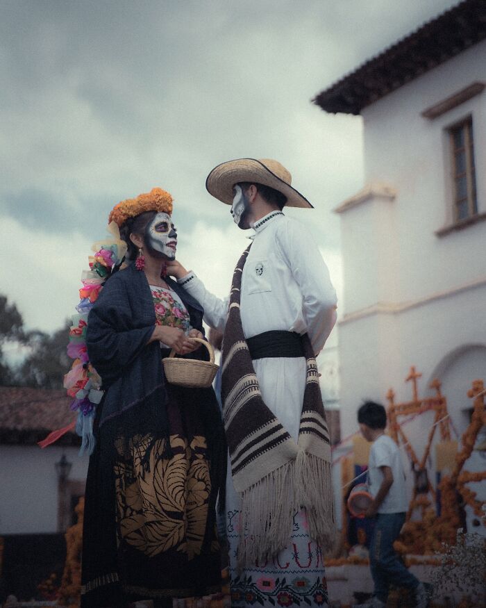 Couple dressed in traditional Day of the Dead attire with painted faces, captured in a striking street photo resembling movie stills.