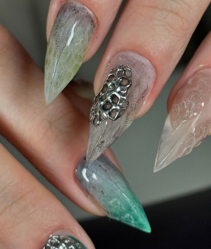 Stiletto nail designs featuring unique textures and metallic accents in muted green and gray tones.