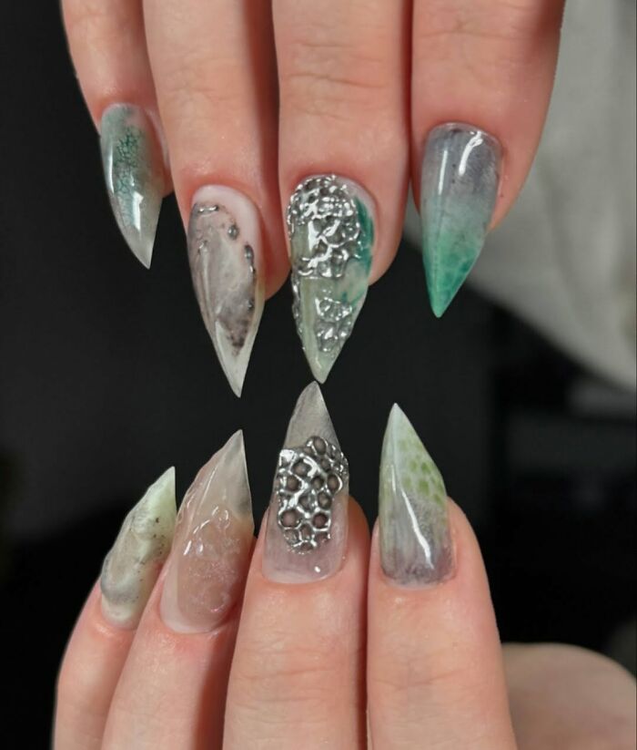 Stiletto nail designs featuring unique textures and metallic accents in muted green and gray tones.