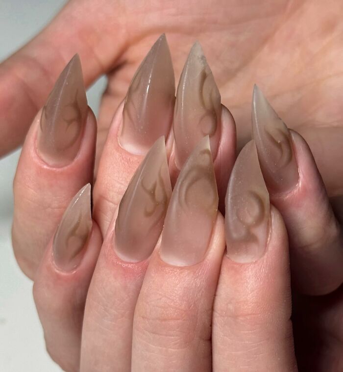 Matte stiletto nail designs in neutral tones with subtle abstract patterns showcasing unique nail art creativity.