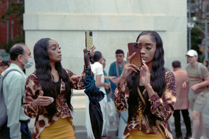 Two striking street photos of a woman with long hair taking selfies in a busy urban setting, resembling movie stills.