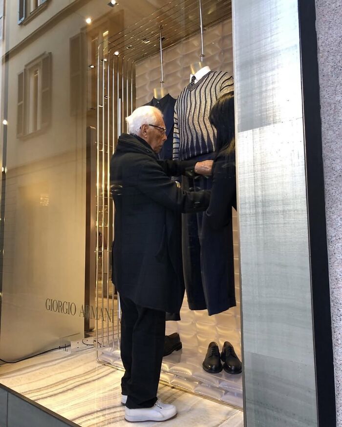 Elderly man adjusting clothing on mannequin in a stylish Giorgio Armani fashion store window display. Elderly man adjusting clothing on mannequin in a stylish Giorgio Armani fashion store window display.