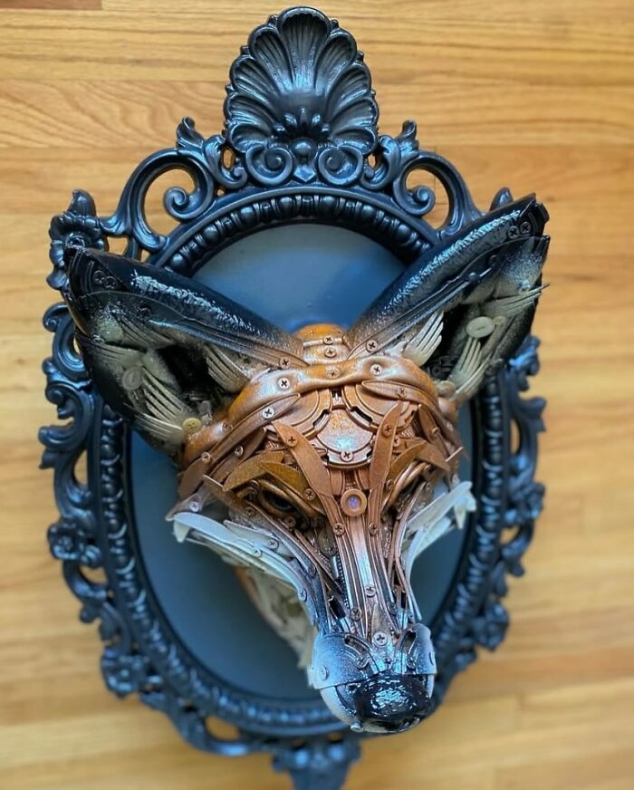 Fox animal sculpture made from recycled trash materials displayed in an ornate black frame on a wooden surface.