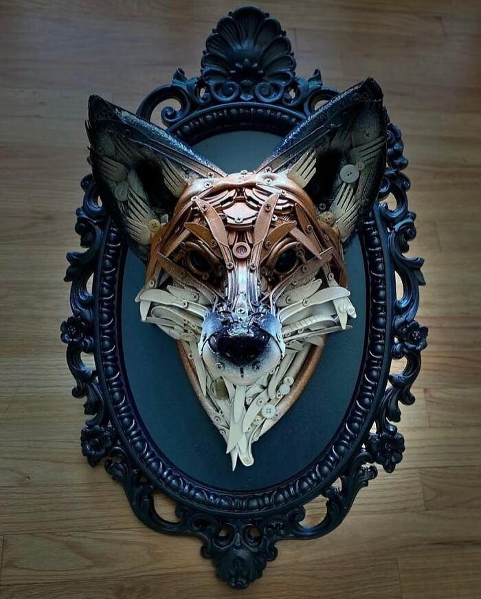 Fox animal sculpture made from recycled trash materials displayed in an ornate black frame on a wooden surface.