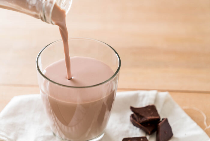 Glass of chocolate milk being poured on a table near pieces of chocolate, illustrating shocking school incidents involving secret affairs.
