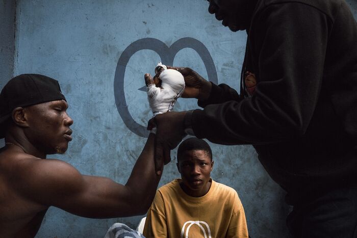 Three young men in a street scene with one wrapping another's hand, capturing a striking photo with cinematic lighting.