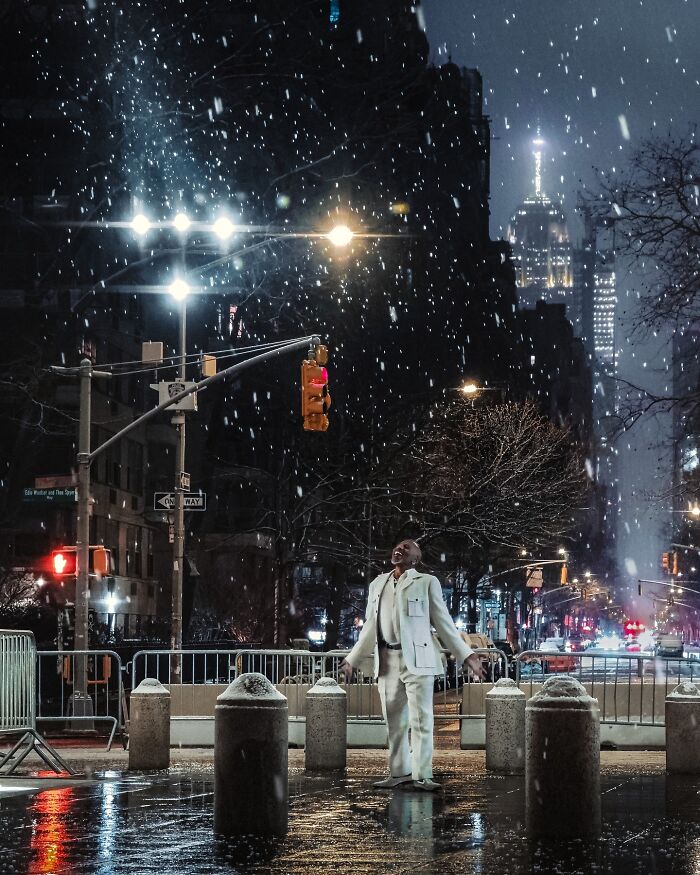 Man in white suit standing under streetlights in snowy city street scene, striking street photo with cinematic feel.