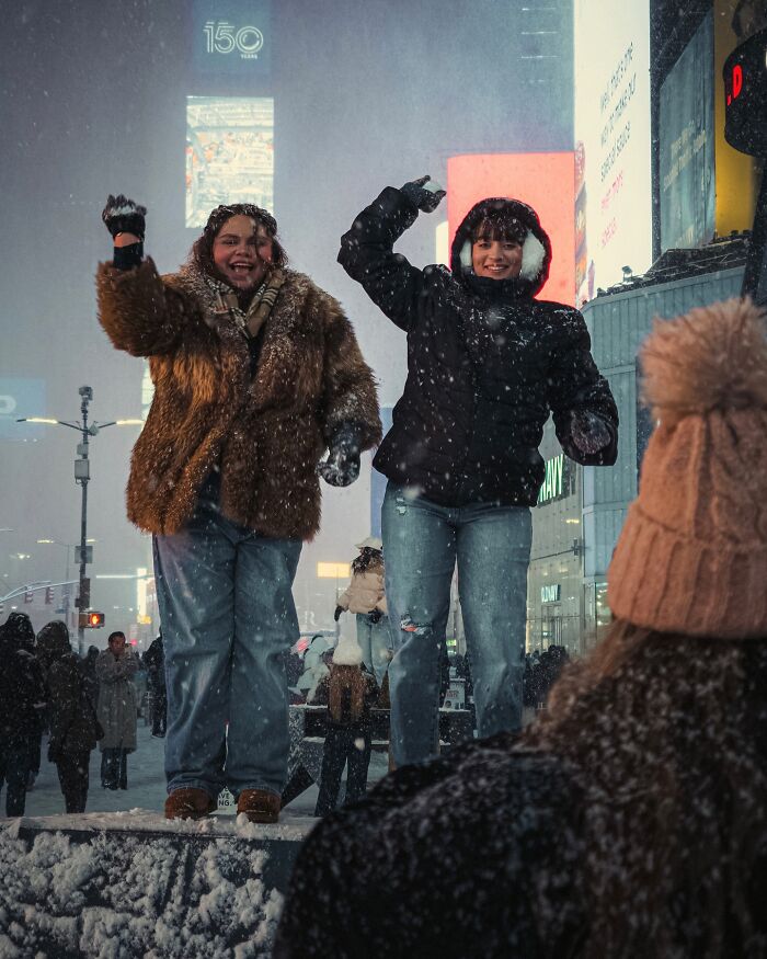 Two people in winter clothes posing joyfully on a snowy street, captured in striking street photos resembling movie stills.