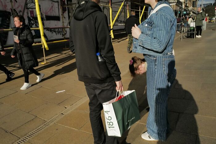 Street photo capturing a humorous moment on a busy urban sidewalk with people engaged in everyday activities.