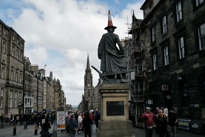 Street photo of a city statue humorously topped with a traffic cone, capturing the funny side of life in public spaces.