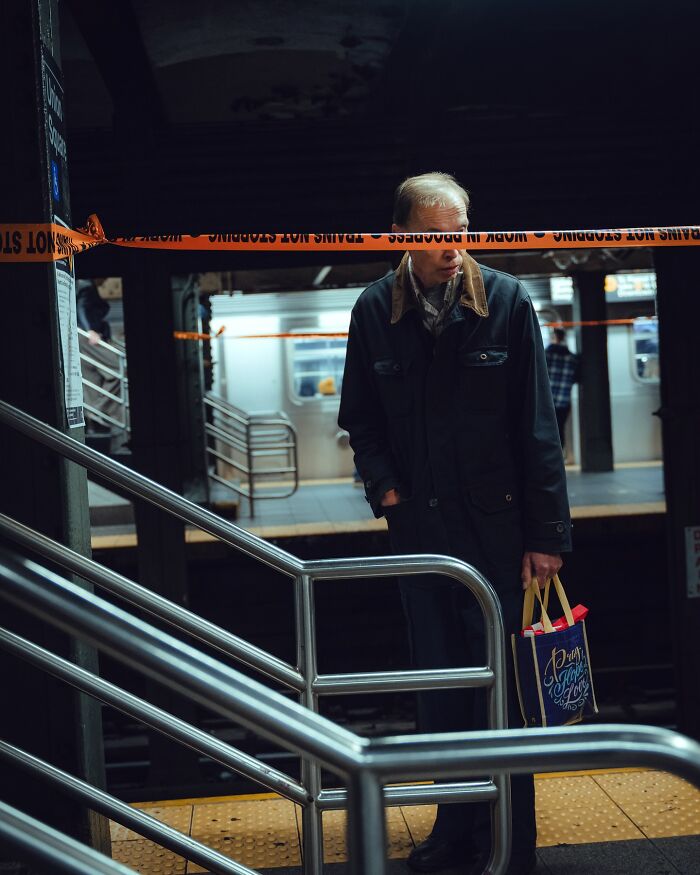 Man standing behind caution tape at subway platform, captured in a striking street photo with cinematic lighting and mood.