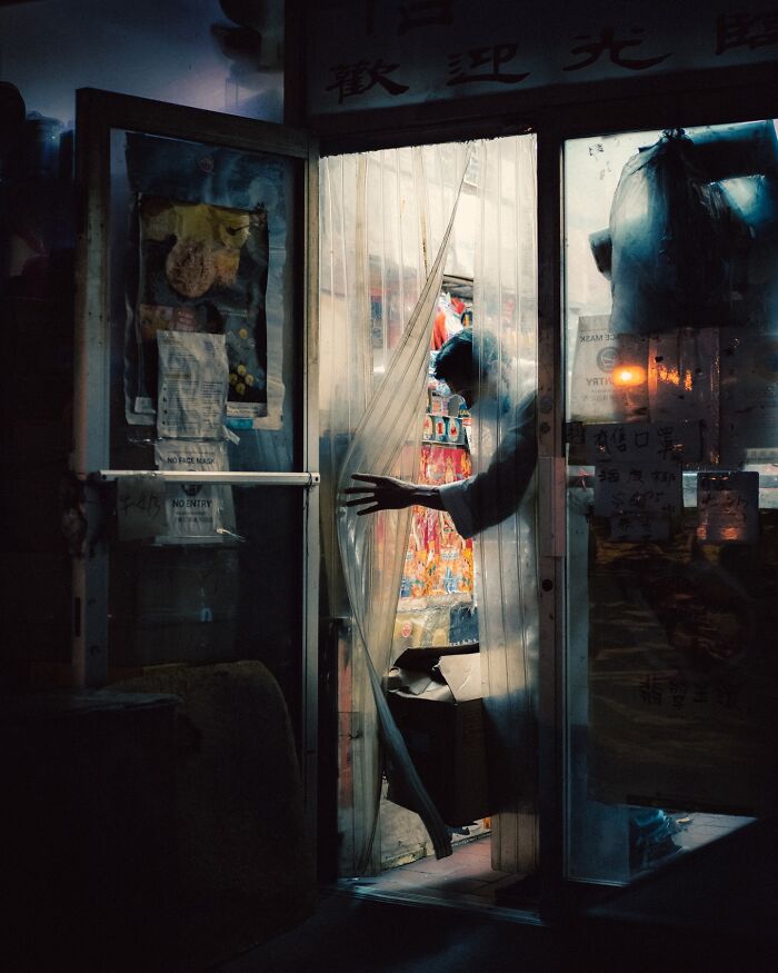 Man opening translucent door in dimly lit shop, striking street photo with cinematic atmosphere and vivid colors.