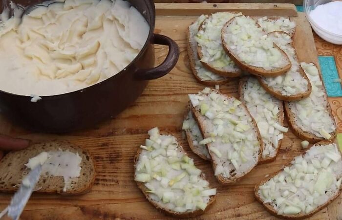 Traditional Eastern European slices of bread topped with chopped onions and a pot of creamy spread on a wooden board.