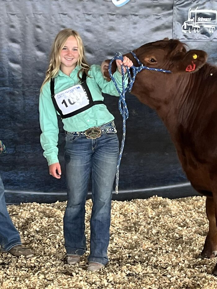 Teenage girl smiling and holding a calf's rope at an agricultural event, reflecting the soul-crushing tragedy of mistaken identity. Teenage girl smiling and holding a calf's rope at an agricultural event, reflecting the soul-crushing tragedy of mistaken identity.