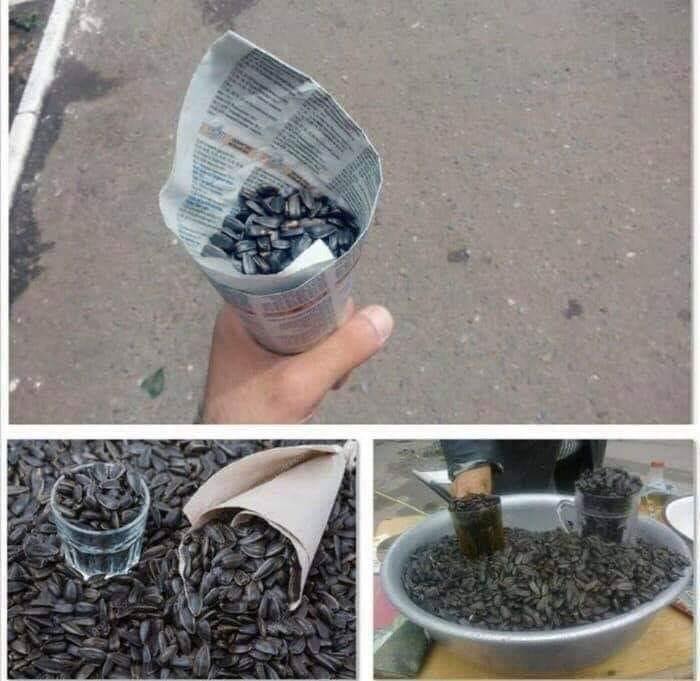 Hand holding sunflower seeds in newspaper cone and large containers full of sunflower seeds, Eastern Europe culture snack.
