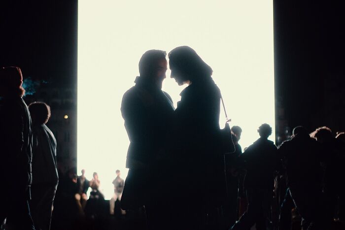 Silhouetted couple in an intimate moment on a busy street illuminated by a bright light, striking street photo scene.