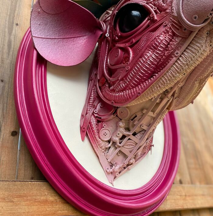Pink animal sculpture made from trash, showcasing intricate details in a creative recycled art piece on a wooden floor.