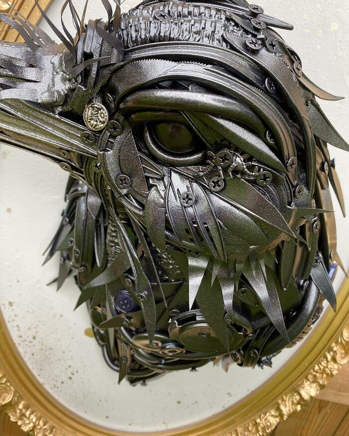 Recycled materials shaped into a stunning black bird sculpture mounted in an ornate gold frame on wooden wall.