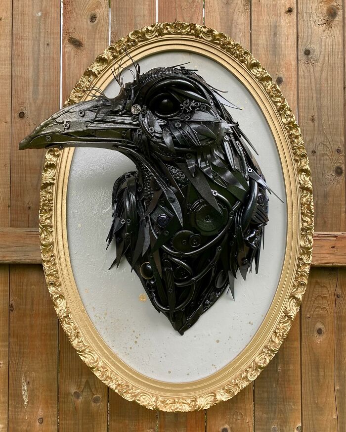 Recycled materials shaped into a stunning black bird sculpture mounted in an ornate gold frame on wooden wall.