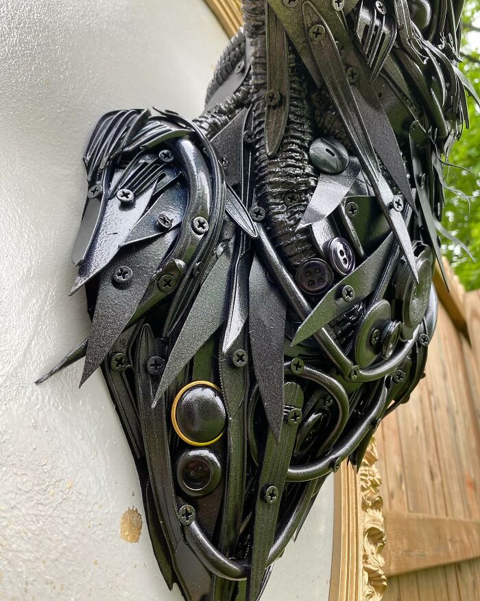 Recycled materials shaped into a stunning black bird sculpture mounted in an ornate gold frame on wooden wall.