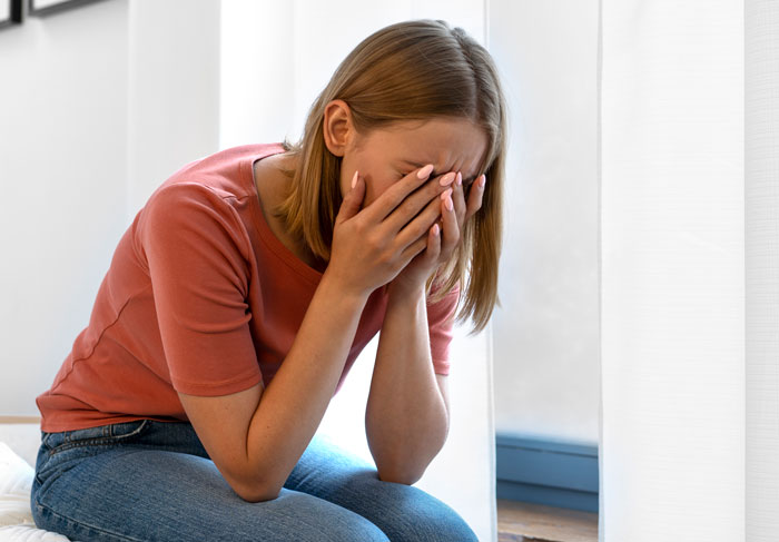 Young woman sitting indoors, covering her face, conveying emotions related to telling wife why daughter doesn&rsquo;t trust.