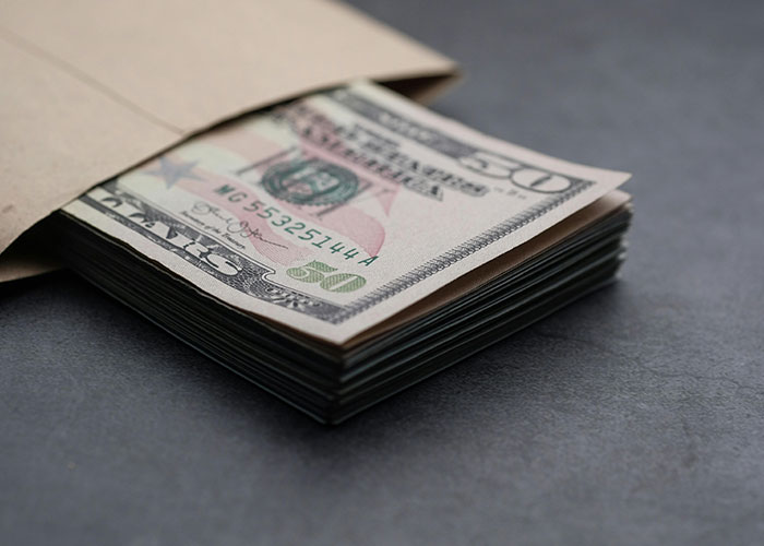 Stack of fifty dollar bills partially inside a brown envelope representing settlement for white oak tree damage case.