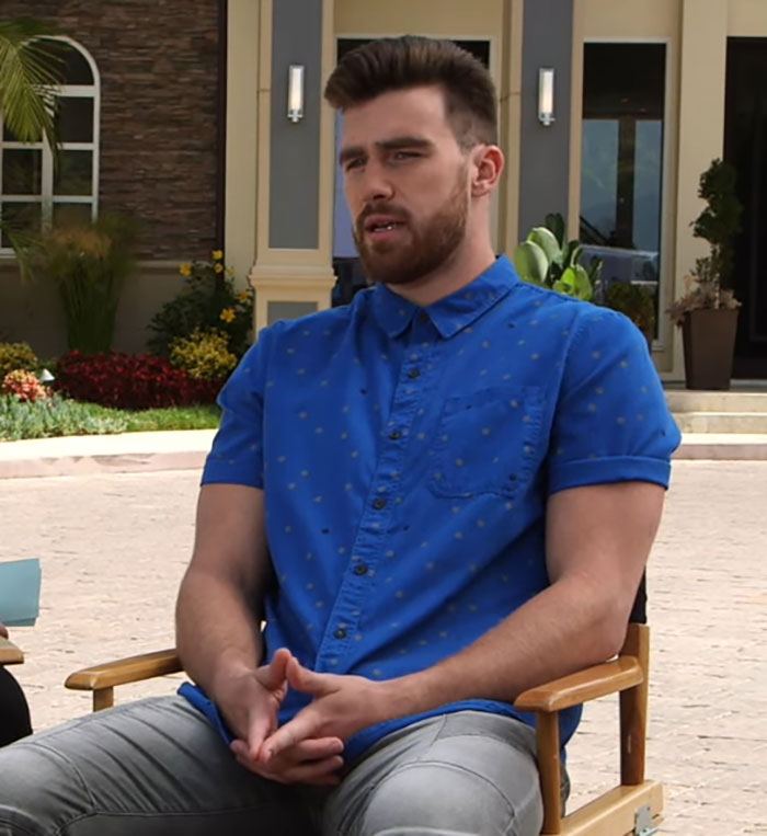 Man in blue shirt sitting outdoors, discussing Travis Kelce&rsquo;s answer about Taylor Swift in a resurfaced video clip.