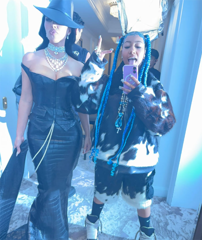 Kim Kardashian and North West posing indoors, North showing middle finger with dermal piercing and phone selfie.