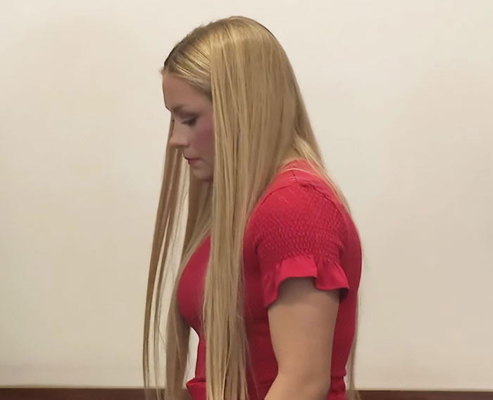 Young cheerleader with long blonde hair, wearing a red top, appearing solemn in an indoor setting related to the news event.