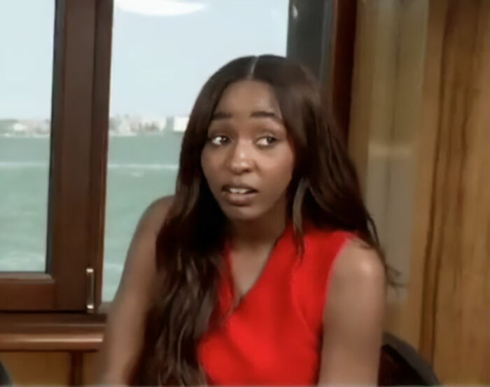 Ayo Edebiri wearing red in an indoor setting, showing a surprised expression near a window with water view.