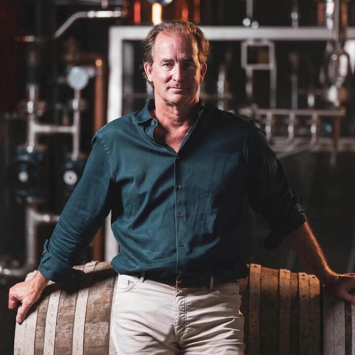 Middle-aged man in a teal shirt leaning on barrels, representing ex-astronomer HR chief Kristin Cabot divorce news.