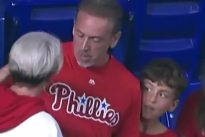 Man in a Phillies shirt talks to woman with white hair while a boy looks on during MLB ball confrontation at stadium.