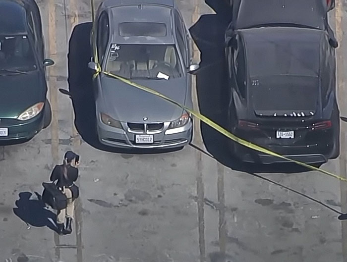 Aerial view of a Tesla car in a parking lot with police tape after decomposing body found in abandoned vehicle.