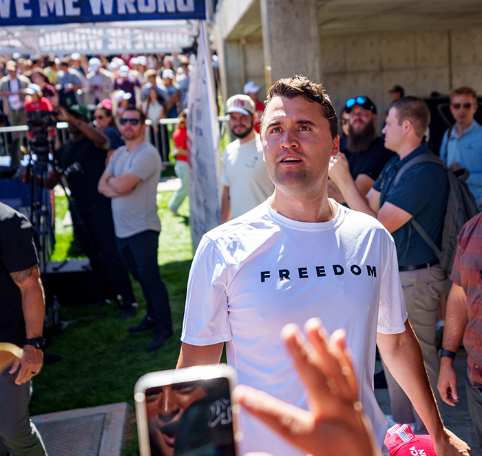 Man wearing a white freedom t-shirt at a crowded outdoor event after Utah tragedy commentator remarks controversy.