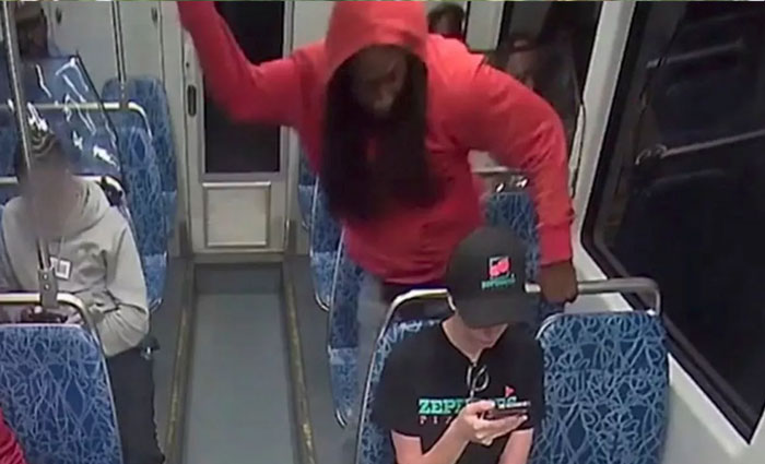 Person in red hoodie raising arm aggressively over seated person on public transit during Ukrainian refugee attack discussion. Person in red hoodie raising arm aggressively over seated person on public transit during Ukrainian refugee attack discussion.