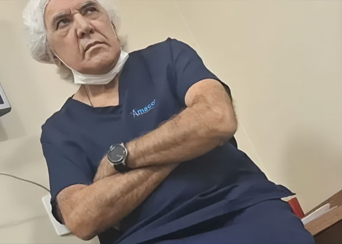 Plastic surgeon in navy scrubs and hairnet with arms crossed, related to mom's butt lift procedure gone wrong.