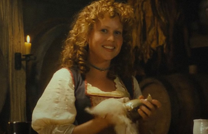 Smiling professor with curly hair in historic attire holding a chicken, creating a memorable impression on students.