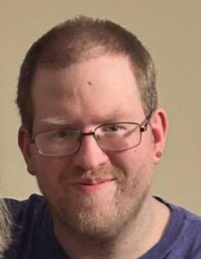 Man with glasses and a beard, headshot photo related to pastor's son accused of disturbing acts against adults held captive.