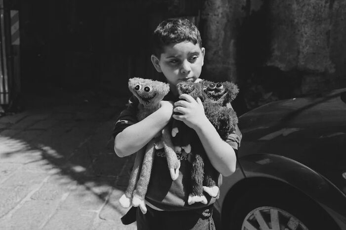 Boy holding three stuffed toys outdoors in a powerful photograph from the children of the world series by Andrea Torrei