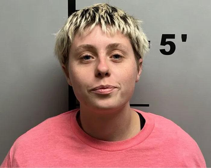 Young woman with short blonde hair wearing a pink shirt in front of a height measurement wall, linked to sisters who destroyed Charlie Kirk memorial.