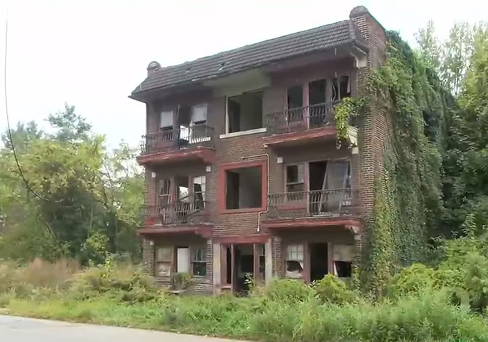Abandoned brick building overgrown with vegetation, setting scene for cop opening fire on teens over porta-potty prank debate.