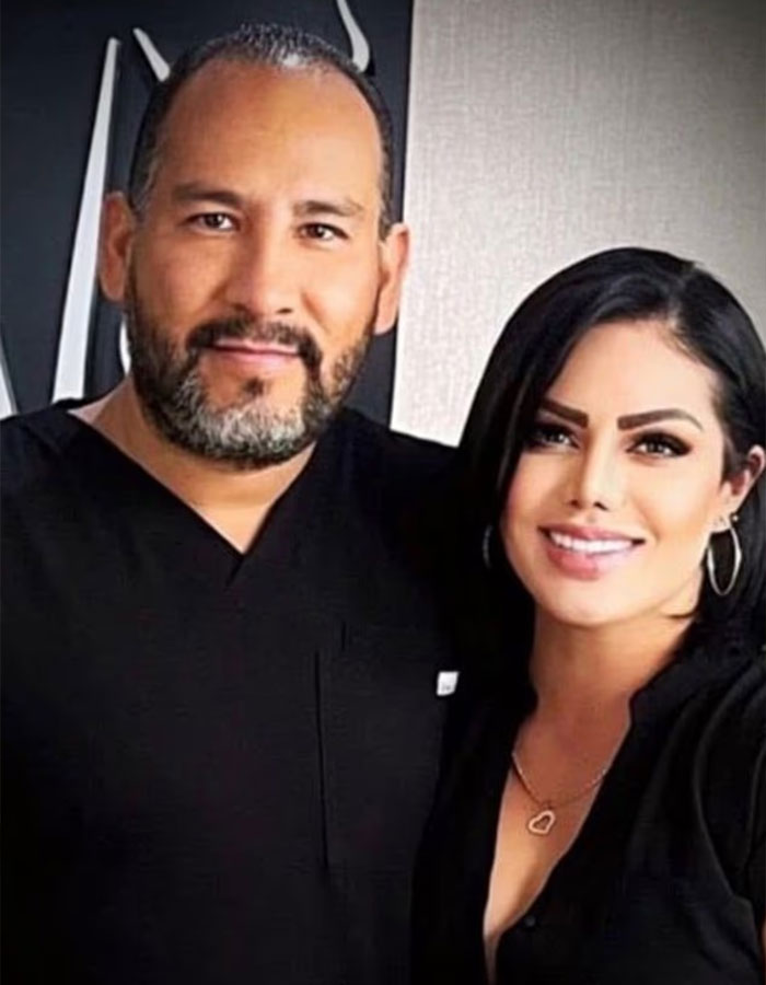 Surgeon who performed fatal breast enlargement and teen&rsquo;s mom posing together, both dressed in black indoors.